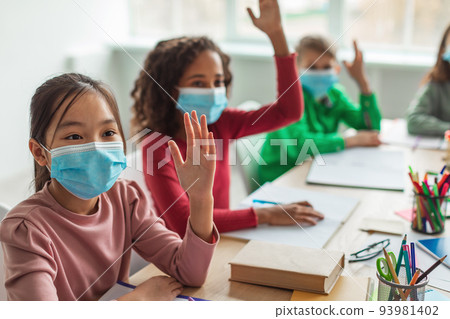 Diverse School Children Wearing Face Masks Raising Arms In Classroom Diverse School Children Wearing Face Masks Raising Arms In Classroom 93981402