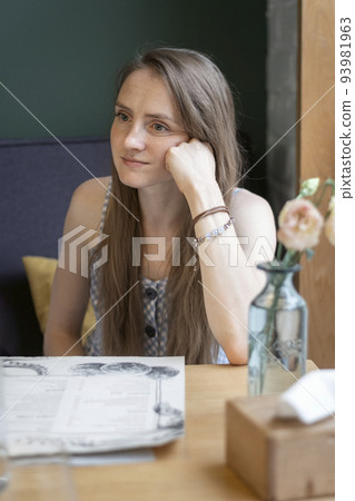 Pensive young woman sits in a cafe with her head resting on her hand. Tired look to nowhere Pensive young woman sits in a cafe with her head resting on her hand. Tired look to nowhere 93981963