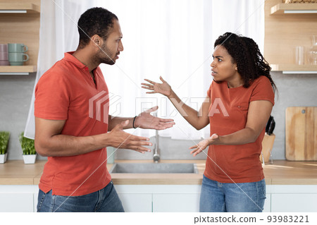 Sad angry young african american guy and lady in same t-shirts quarrel and gesticulate in kitchen interior 93983221