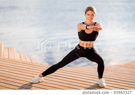 Sporty middle aged female in activewear making side lunges exercise outdoors 93983327
