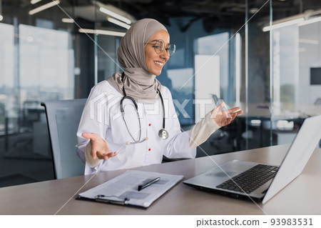 Doctor online consultation with patient, muslim woman in hijab working remotely with laptop for video call, consulting patients sitting inside modern clinic office Doctor online consultation with patient, muslim woman in hijab working remotely with laptop for video call, consulting patients sitting inside modern clinic office 93983531