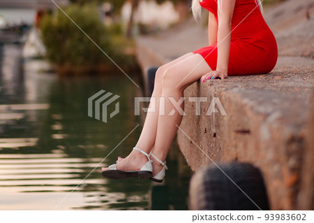 Elegant female legs in tights, sandals and a red skirt sitting the pier, close-up. The concept of epilation, weight loss and hair removal 93983602