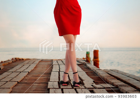Elegant female legs in tights, heeled sandals and a red skirt on the pier, close-up. Sea and sky in the background. The concept of epilation, weight loss and hair removal 93983603