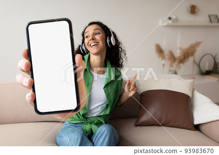 Music App. Cheerful Young Woman In Wireless Headphones Holding Big Blank Smartphone 93983670