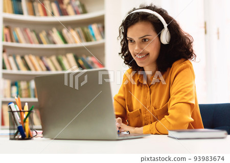 Happy mixed race woman in headphones studying online with laptop in library interior, watching webinar, copy space 93983674