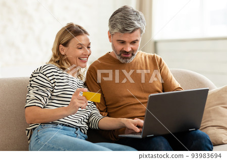 Couple Shopping Online Using Credit Card And Laptop At Home 93983694
