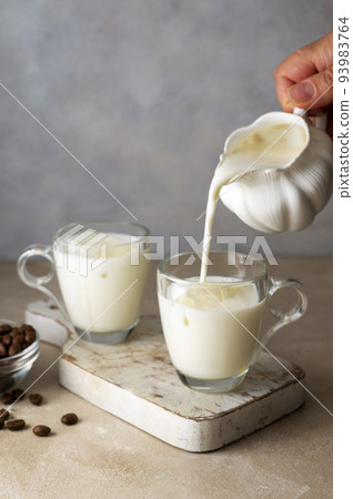 Pouring milk in glass cups with ice to prepare dalgona coffee. Step by step recipe. 93983764
