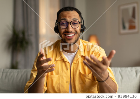 Young African American guy in headphones having online meeting, participating in webinar or business conference at home Young African American guy in headphones having online meeting, participating in webinar or business conference at home 93984136