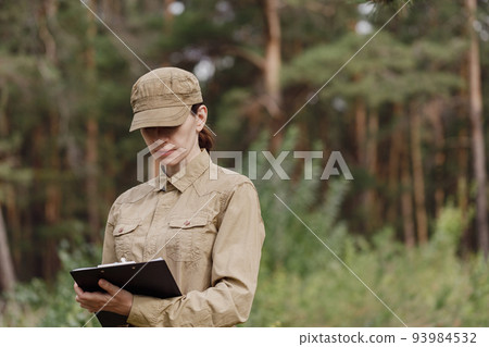 A woman biologist in uniform with a clipboard explore the forest biocenosis in national park in summer, selective focus. 93984532