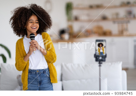 Positive black girl singing and recording video on mobile phone Positive black girl singing and recording video on mobile phone 93984745