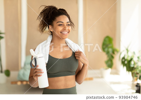 Portrait of happy black woman in sportswear and white towel on neck holding bottle with fresh water, copy space Portrait of happy black woman in sportswear and white towel on neck holding bottle with fresh water, copy space 93984746