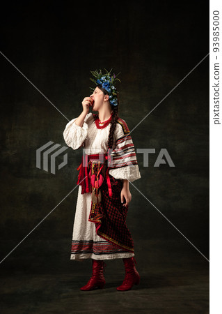 Art portrait of beautiful woman wearing traditional folk Ukrainian costume posing isolated over dark vintage background. Fashion, beauty, cultural heritage Art portrait of beautiful woman wearing traditional folk Ukrainian costume posing isolated over dark vintage background. Fashion, beauty, cultural heritage 93985000