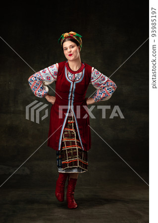 Art portrait of beautiful woman wearing traditional folk Ukrainian costume posing isolated over dark vintage background. Fashion, beauty, cultural heritage 93985197