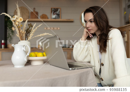 young woman sitting at the table looks into the laptop under the first hand young woman sitting at the table looks into the laptop under the first hand 93988135