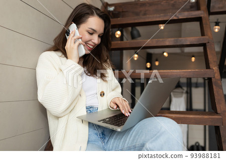 young woman with a smile on her face talking on the phone and making an order while looking at a 93988181