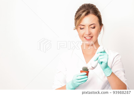 A smiling female beautician holds little green cactus with the razor in her hands. Hair removal concept 93988287