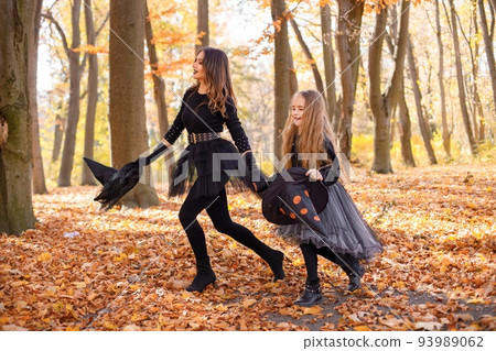 Woman with little girl walking in autumn forest. Mother play with her daughter. Mother and daughter wearing witches Halloween costumes and cone hats. 93989062