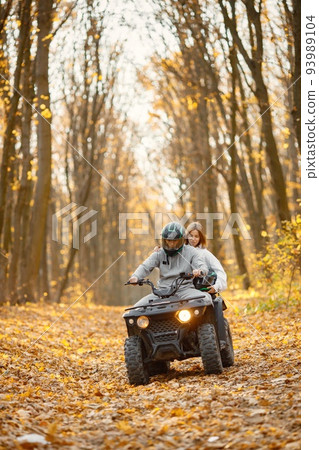 A young caucasian man and woman riding an ATV quad bike in autumn forest. Couple maneuvering off-road ATV. Couple wearing grey sportive costumes. A young caucasian man and woman riding an ATV quad bike in autumn forest. Couple maneuvering off-road ATV. Couple wearing grey sportive costumes. 93989104
