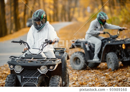 Focus on a woman riding an ATV quad bikes in autumn forest. Two friends maneuvering off-road ATV. Couple wearing grey sportive costumes. Focus on a woman riding an ATV quad bikes in autumn forest. Two friends maneuvering off-road ATV. Couple wearing grey sportive costumes. 93989168