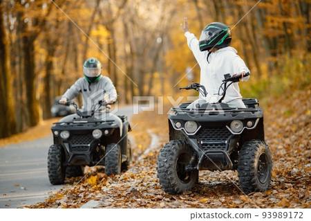 A young caucasian man and woman riding an ATV quad bikes in autumn forest. Two friends maneuvering off-road ATV. Couple wearing grey sportive costumes. A young caucasian man and woman riding an ATV quad bikes in autumn forest. Two friends maneuvering off-road ATV. Couple wearing grey sportive costumes. 93989172