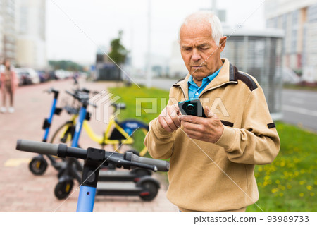 Senior man with smartphone activating electric scooter Senior man with smartphone activating electric scooter 93989733
