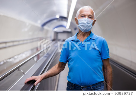 Retired man in protective mask walking down the escalator to metro station 93989757