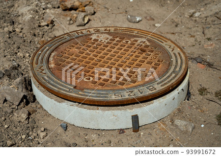 Rusty round sewer hatch on construction site. 93991672