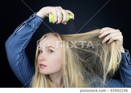 Dry shampoo. Blonde girl sprays shampoo on her hair. The problem of oily hair while traveling. An emergency remedy for excessive sebum production. Make your head clean without water 93992246