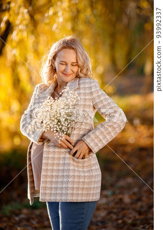 Portrait of middle-aged pregnant woman outdoors at park. Middle age pregnant woman expecting baby at aged pregnancy. Blonde woman wearing brown sweater and beige coat. Portrait of middle-aged pregnant woman outdoors at park. Middle age pregnant woman expecting baby at aged pregnancy. Blonde woman wearing brown sweater and beige coat. 93992337