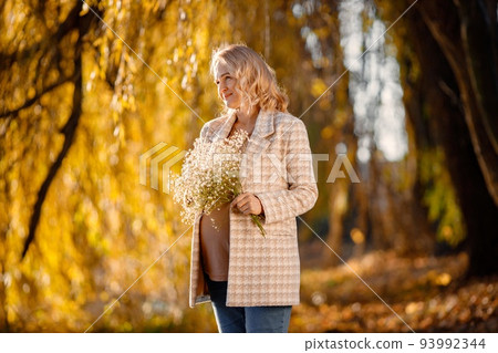 Portrait of middle-aged pregnant woman outdoors at park. Middle age pregnant woman expecting baby at aged pregnancy. Blonde woman wearing brown sweater and beige coat. Portrait of middle-aged pregnant woman outdoors at park. Middle age pregnant woman expecting baby at aged pregnancy. Blonde woman wearing brown sweater and beige coat. 93992344
