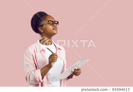 Young African American woman student wearing glasses holds clipboard stands in pink studio 93994615