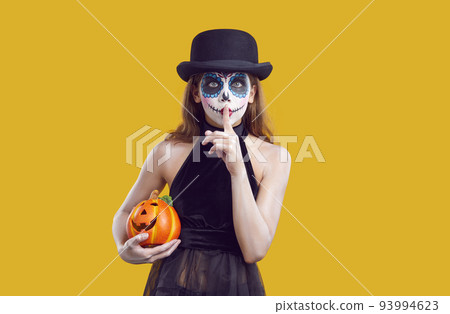 Woman in halloween costume with scary makeup in hat showing silence gesture on yellow background. 93994623