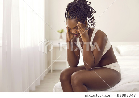 Tired stressed young black woman who is suffering from headache sitting on bed at home Tired stressed young black woman who is suffering from headache sitting on bed at home 93995348