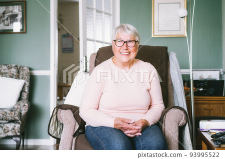 Portrait of smiling senior, mature retired grandmother in eyeglasses, elderly woman smiling, sitting on the armchair at home enjoying retirement. Selective focus. Portrait of smiling senior, mature retired grandmother in eyeglasses, elderly woman smiling, sitting on the armchair at home enjoying retirement. Selective focus. 93995522