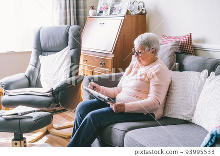 Old senior woman, 80s adult, grandmother, making crossword puzzles in her living room sitting on the sofa. Retirement hobby for training memory. Alzheimer's preventive practice. Selective focus Old senior woman, 80s adult, grandmother, making crossword puzzles in her living room sitting on the sofa. Retirement hobby for training memory. Alzheimer's preventive practice. Selective focus 93995533