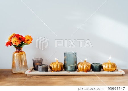 Autumn, fall cozy composition. Fresh dahlia flowers in vase and pumpkin shaped golden candles on the wooden tray with white wall background. Scandinavian minimalist hygge home decor. Selective focus Autumn, fall cozy composition. Fresh dahlia flowers in vase and pumpkin shaped golden candles on the wooden tray with white wall background. Scandinavian minimalist hygge home decor. Selective focus 93995547