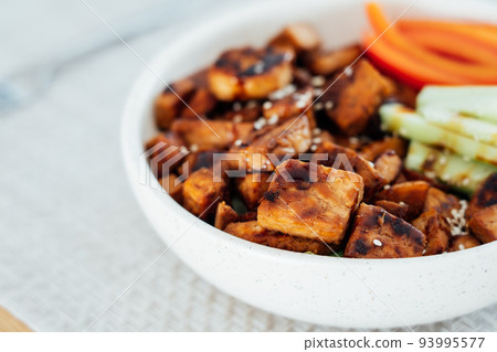 Closeup Bowl with roasted tempeh made of fermented soy beans, fresh vegetable sticks with sauce and sesame seeds on table. Plant based protein. Healthy cooking and eating. Go vegan. selective focus. Closeup Bowl with roasted tempeh made of fermented soy beans, fresh vegetable sticks with sauce and sesame seeds on table. Plant based protein. Healthy cooking and eating. Go vegan. selective focus. 93995577