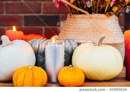 Festive composition for autumn holidays. Burning candle, various pumpkins and flowers bouquet in the wicker basket on brik wall background. Thanksgiving or Halloween. Fall Harvesting. Selective focus 93995634