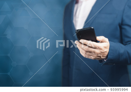 man in a suit is holding mobile cellphone. Online business. businessman holding the phone on dark blue blurred background. copy space man in a suit is holding mobile cellphone. Online business. businessman holding the phone on dark blue blurred background. copy space 93995994
