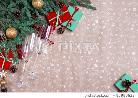 Christmas decor on a art paper background. Christmas fir branches, gift boxes with red ribbon, red decoration, sparkles and champagne glasses 93996622