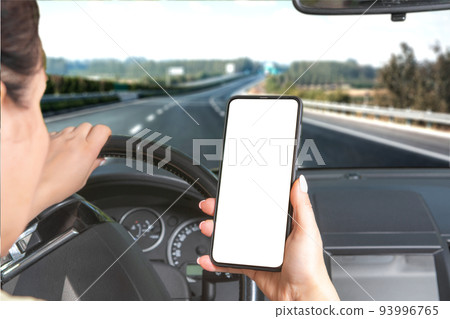 Young woman holding blank screen cell phone while driving car. Mockup phone. Car is speeding along the highway. Young woman holding blank screen cell phone while driving car. Mockup phone. Car is speeding along the highway. 93996765