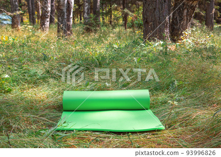 Yoga mat on grass in nature, against the background of a pine forest. yoga in nature concept Yoga mat on grass in nature, against the background of a pine forest. yoga in nature concept 93996826