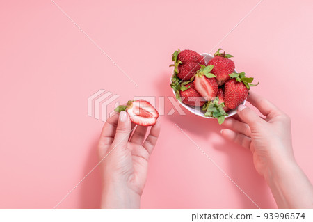 Close-up fresh peeled strawberry in white bowl on pink background. A woman's hand takes strawberries from a bowl. Close-up fresh peeled strawberry in white bowl on pink background. A woman's hand takes strawberries from a bowl. 93996874