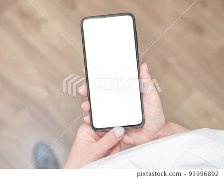 Woman stands and holds a mobile phone with a blank screen in her hands. 93996892