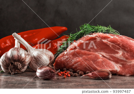 raw meat and spices still life. Piece of raw meat ready for preparation with greens and spices. Dark wooden background. 93997487