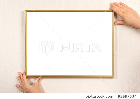 Golden blank picture frame hanging on a beige wall. Hands hanging photo frame mockup on wall Golden blank picture frame hanging on a beige wall. Hands hanging photo frame mockup on wall 93997534