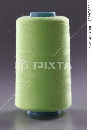 Light green spool of thread on gray background Light green spool of thread on gray background 93997605