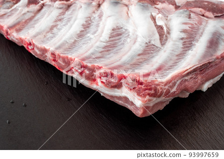 Whole raw pork ribs isolated on dark, black, stone board. spare ribs or belly. close-up Whole raw pork ribs isolated on dark, black, stone board. spare ribs or belly. close-up 93997659