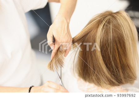 Woman hairdresser cuts hair with scissors in barbershop Woman hairdresser cuts hair with scissors in barbershop 93997692