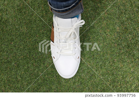 Man is wearing white sneakers on green lawn grass Man is wearing white sneakers on green lawn grass 93997756